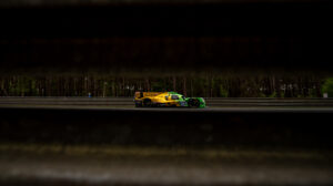 Green and yellow racing car drives along an empty track at night-time.