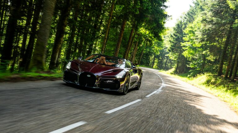 The Bugatti W16 Mistral on a test drive on a quiet country road with tall evergreen trees down each side.