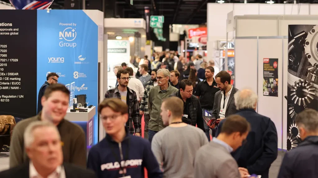 The busy show floor or PMW Expo exhibition, with people walking between long cordidor or stalls and stands.