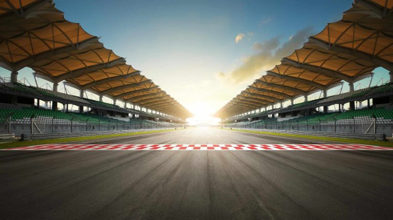 A empty race track with the sun setting in the far distance at the end of the home straight.