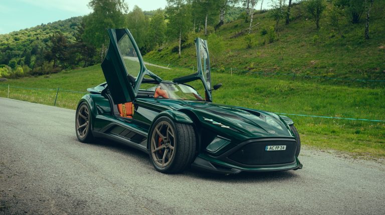 Donkervoort introduces right-hand-drive P24 RS A dark green right-hand-drive Donkervoort P24 RS with its doors open. It is parked on a quiet rural road with grass and trees in the background.