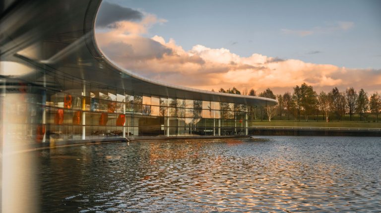 McLaren Automotive expands UK operations with £500m investment External view of the McLaren Production Centre in Woking, UK, with glass offices and a water feature.