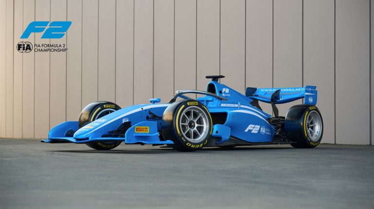 The new Formula 2 race car. It is blue and parked on the asphalt at a racetrack. It has FIA, Pirelli, Aramco and Dallara logos. The F2 logo is in the top left hand corner of the photo.
